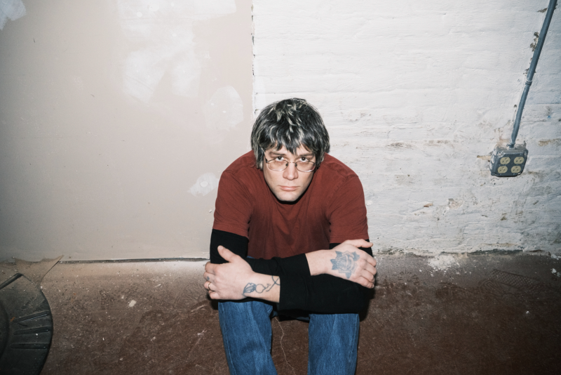 Greg sits on the floor against a beige and white wall.