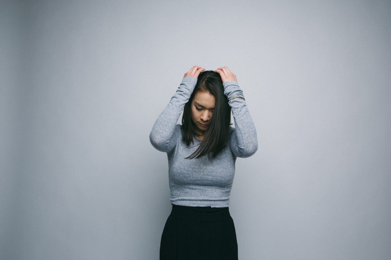 Mitski standing against a white backdrop holding her head